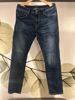 Mörkblå Jack & Jones Jeans straight fit - Snygga mörkblå straight fit jeans från Jack & Jones med klassisk femficksdesign och subtila slitningar framtill. Jeansen har raka ben och är tillverkade i stretchigt denim för extra komfort. Perfekta till en avslappnad streetwear-look.
