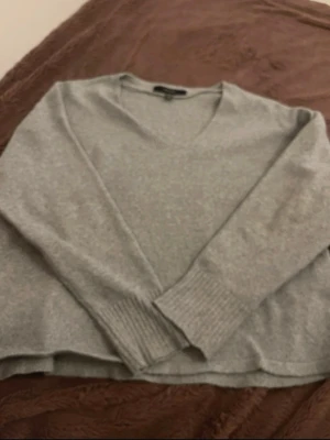 Ljusgrå stickad tröja med v-ringning - En enkel och stilren ljusgrå stickad tröja med v-ringad hals och långa ärmar. Tröjan har ribbade muddar vid ärmslut och nederkant. Perfekt att matcha med jeans eller kjol för en avslappnad look.