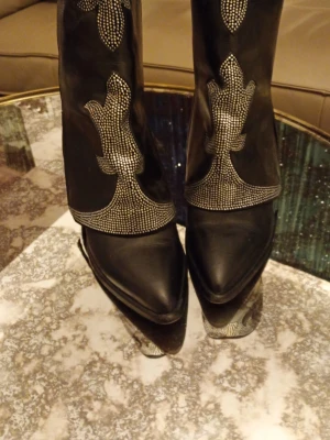 Svarta cowboy boots med nitar Elena iatchi  - Snygga svarta cowboy boots från Paris Elena iatchi med spetsig tå och dekorativa silverfärgade nitar i mönster på skaftet. Tillverkade i läder med robust klack och klassisk westernstil. Perfekta för dig som vill sticka ut med coola detaljer.