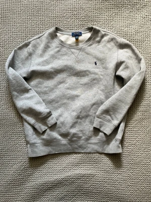 Grå sweatshirt från Polo Ralph Lauren - Klassisk grå crewneck från Polo Ralph Lauren med rund halsringning och broderad marinblå logga på bröstet. Mjuk insida och snygg design vilket gör den mycket enkel att bära. Den är 14-16 / L i barnstorlek vilket i vuxenstorlek motsvarar XS.