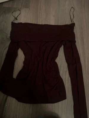 Mörkröd off shoulder topp - Trendig mörkröd off shoulder topp med långa ärmar och tunna axelband. Sitter tight och har en bred kant upptill som ger en snygg siluett. Perfekt att styla med jeans eller kjol för en cool look.