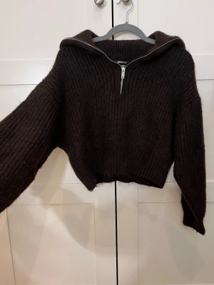 Mörkbrun stickad tröja med dragkedja - Mysig mörkbrun stickad tröja från Gina Tricot med bred krage och halv dragkedja framtill. Tröjan har en croppad passform, ribbstickat material och långa ärmar. Perfekt för lager på lager och en avslappnad look. Detta är en kort tröja som är använd i storlek M. Kan gå ner i pris. 