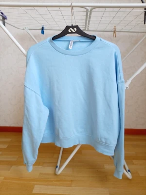 Ljusblå oversized sweatshirt - Ljusblå oversized sweatshirt med rund halsringning och ribbade muddar vid ärmslut och nederkant. Tröjan har en avslappnad passform och är tillverkad i mjukt bomullsmaterial. Perfekt för en chill och casual look.