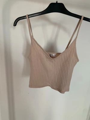 Beige/ljusrosa ribbad linnetopp från Divided - Säljer en beige/ljusrosa ribbad linnetopp från Divided med smala axelband och v-ringad hals. Toppen är croppad och har en enkel, stilren look som passar perfekt till jeans eller kjol.
