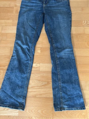 Blå bootcut jeans i klassisk denim - Ett par blå bootcut jeans i klassisk denim med lätt tvättad look. Jeansen har mid midja och vida ben från knät och ner. Perfekta för dig som gillar retrostil och vill ha ett par bekväma jeans med snygg passform.