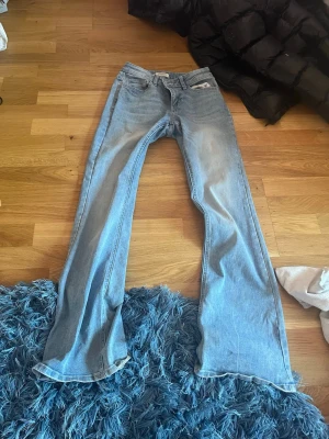Ljusblå bootcut jeans - Säljer ett par ljusblå bootcut jeans med klassisk femficksdesign och normal midja. Jeansen har en avslappnad passform över låren och utsvängda ben. Perfekta för en trendig och avslappnad stil.