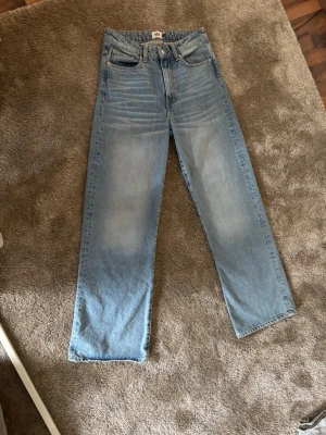 Två par raka jeans i olika tvättar s, 34 - Säljer två par raka jeans, ett par i ljusblå tvätt och  hög midja (Lager157 s), och ett par i ljusgrå tvätt med låg midja (Gina Perfect jeans 34). Båda har klassisk femficksdesign och är tillverkade i bomullsdenim. Perfekta för en avslappnad och trendig look. Bägge för 150kr