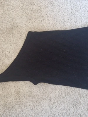 Svart oneshoulder topp från Kappahl - Snygg svart oneshoulder topp från Kappahl i ribbad kvalitet. Perfekt för dig som vill ha en enkel men trendig topp med unik skärning. Passar till många olika stilar och är lätt att matcha med både jeans och kjol.