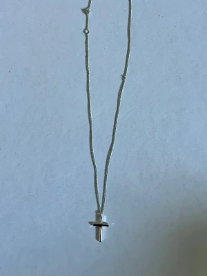 Silverhalsband med kors från Pilgrim - Snyggt silverfärgat halsband från märket Pilgrim med ett minimalistiskt kors som hänge. Kedjan är tunn och smidig, och har även en liten bricka med Pilgrim-loggan vid låset. Perfekt för dig som gillar stilrena accessoarer med en personlig touch. För er silver älskare! Priset är absolut diskuterbart