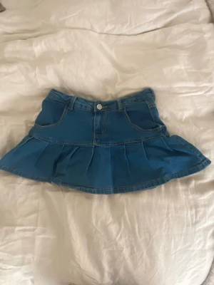 Blå jeanskjol med volang - Säljer en söt blå jeanskjol med volangkant och fickor fram, med insydda shorts. Står storlek S men skulle säga att den är mer som en xs.  Bra skick!!