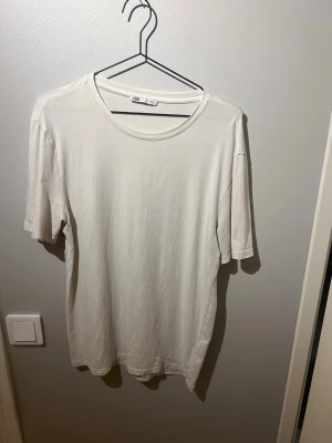 Vit  t-shirt från Zara - En enkel och stilren vit t-shirt från Zara med rund halsringning och normal passform. Tillverkad i mjuk bomull som känns skön mot huden. Perfekt att matcha med jeans eller shorts för en clean look.