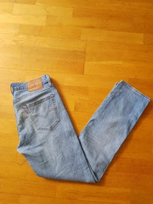Levi's ljusblå raka jeans - Klassiska ljusblå jeans från Levi's med rak passform och hög midja. Jeansen har fem fickor, Levi's ikoniska läderpatch bak och röd logotagg på bakfickan. Tillverkade i slitstark denim, perfekta för en avslappnad och tidlös stil.