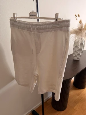 Vita shorts med snörning från BOSS - Säljer ett par stilrena vita shorts från BOSS med elastisk midja och snörning. Shortsen har fickor på sidorna och är tillverkade i mjukt bomullsmaterial. Perfekta för sommardagar och chill häng.