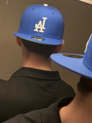 New Era Keps - Snygg blå keps från New Era med LA Dodgers-logga broderad i vitt framtill. Klassisk 59FIFTY-modell med rak skärm och klistermärke kvar på ovansidan. Perfekt för dig som vill ha en sportig och trendig look.