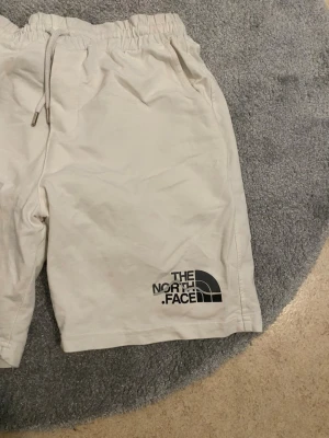 Vita shorts från The North Face - Snygga vita shorts från The North Face med elastisk midja och snörning. De har en avslappnad passform och är perfekta för sommaren. Stort logotryck på ena benet ger en cool streetkänsla. Tillverkade i mjuk bomull för maximal komfort.