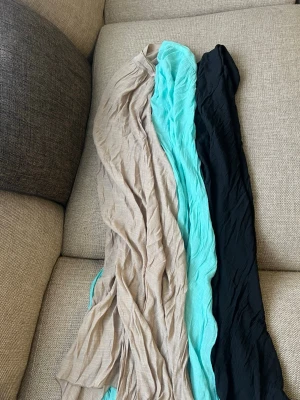 Tre strandkjolar i olika färger - Säljer tre strandkjolar, turkos och svart. Alla är långa och har en lätt, skrynklig struktur som gör dem enkla att styla på olika sätt. Perfekta att slänga över för en snygg touch till din stand outfiten
