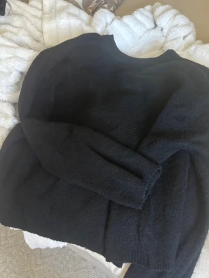 Svart stickad tröja i enkel modell - Mysig svart stickad tröja med rund hals och långa ärmar. Tröjan har en klassisk, rak passform och ribbstickade muddar vid ärmslut och nederkant. Perfekt basplagg för kyligare dagar.