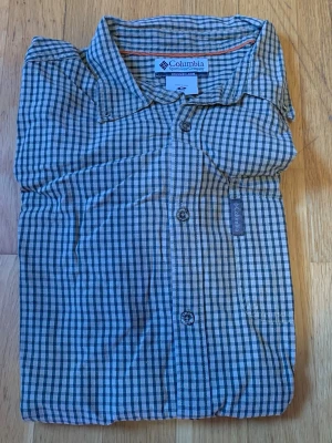 Rutig skjorta från Columbia - Klassisk rutig skjorta från Columbia i blått, gult och vitt. Skjortan har lång ärm, knappar framtill och en avslappnad krage. Tillverkad i lätt bomullsmaterial, perfekt för en casual och bekväm stil.