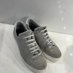 Gråa sneakers från Jacob Cohen - Stilrena gråa sneakers från Jacob Cohen i mocka med vita snören och vit sula. Klassisk låg modell med diskret logga på snörningen. Använda en del men inga defekter. Hör av er vid funderingar! Nypris 6000kr