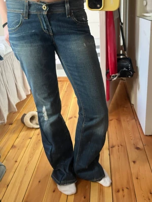 Blå bootcut jeans med slitningar - Säljer ett par blå bootcut jeans med snygga slitningar och kontrastsömmar. Jeansen har klassisk femficksdesign och låg midja. Materialet är denim i bomull med lite stretch för skön passform. Perfekta för en avslappnad och trendig look. Har sytt ut de till bootcut själv. 💕