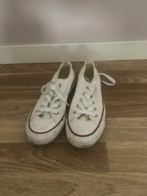 Vita Converse låga sneakers - Klassiska vita Converse sneakers i lågt snitt med vit canvas, vita skosnören och gummisula. Röd rand längs sulan ger en ikonisk look. Perfekta för en avslappnad och stilren outfit.