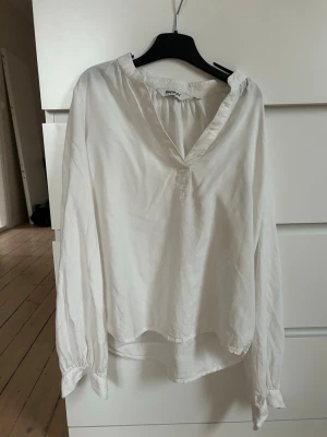 Vit v-ringad blus från Kappahl - Stilren vit blus från Kappahl med v-ringning och långa ärmar. Blusen har en avslappnad passform och är tillverkad i ett mjukt, lätt material som ger ett elegant fall. Perfekt att matcha med jeans eller kjol för en trendig look. Behöver nog strykas men annars hur bra skick som helst!