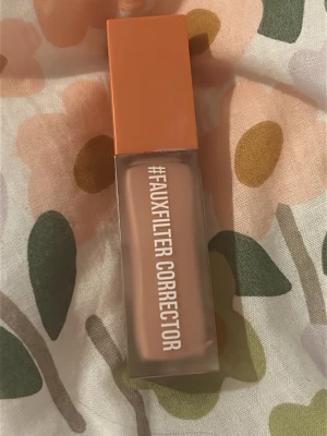 Huda Beauty FauxFilter Corrector - Säljer en Huda Beauty #FauxFilter Corrector concealer med matt finish. Produkten har en varm, persikotonad färg som passar perfekt för att neutralisera mörka ringar under ögonen. Produkten är i nyansen Pink Pomelo. 