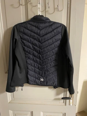 Svart vindjacka från Dobsom - Snygg svart vindjacka från Lager 157 med vadderade partier i chevronmönster på fram- och baksida. Jackan har hel dragkedja, hög krage och släta ärmar i stretchigt material. Perfekt för blåsiga dagar och enkel att matcha med olika outfits.
