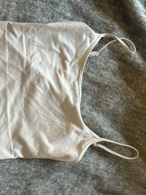 Beige linnetopp med smala axelband - En enkel och stilren beige linnetopp med smala axelband. Toppen har en rak passform och är tillverkad i mjukt bomullsmaterial som känns skönt mot huden. Perfekt att matcha med jeans eller kjol för en clean look.