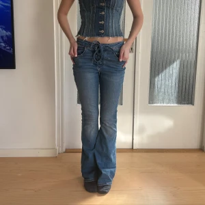 Blå bootcut jeans med snörning - Säljer ett par blå bootcut jeans med unik snörning i midjan och klassiska fem fickor. Jeansen har en lätt utsvängd passform och cool vintagekänsla. Perfekta för dig som vill sticka ut med detaljer och gillar retrostil. Jag har oftast 36 och pris kan diskuteras. 