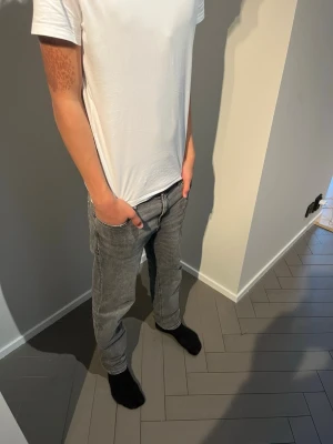 Jack and Jones Jeans - Säljer ett par stilrena grå jeans med klassisk femficksdesign och normal passform. Jeansen har en rak siluett och är perfekta för en avslappnad och trendig look. Passar till det mesta och är ett måste i garderoben. Modellen i bild är 184.