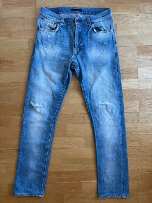 Nudie Jeans - Ljusblå jeans från Nudie Jeans med slitningar och distressed detaljer på låren och knäna. Klassisk femficksmodell med raka ben och orangea sömmar. Perfekta för en avslappnad och trendig look. Hör av dig vid intresse 🙌