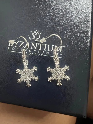 Silvriga snöflingeörhängen  - Säljer ett par glittriga örhängen. Örhängena är formade som snöflingor i silverfärg med små gnistrande stenar som ger extra bling. Perfekta för dig som vill ha en vintrig och unik accessoar till din look. Fick dessa av min mamma men jag använder inte silver så dessa har aldrig använts!
