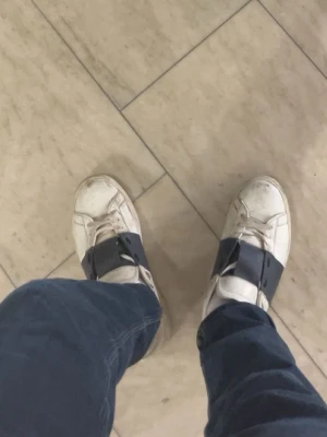 Vita sneakers med blåa detaljer - Säljer ett par vita sneakers med breda mörkblåa kardborreband över vristen. Skorna har en klassisk låg profil och rundad tå. Passar perfekt till jeans eller andra avslappnade outfits.