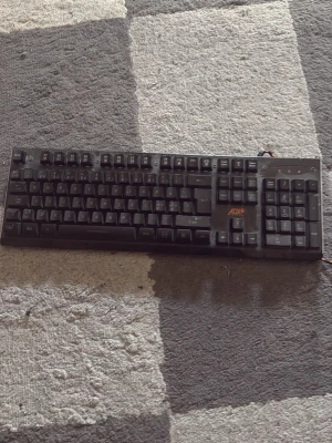 Svart tangentbord från ADX - Säljer ett svart tangentbord från ADX med fullstora tangenter och numerisk del. Tangentbordet har en robust design i plast och ansluts med en flätad USB-kabel i svart och orange. Perfekt för gaming eller vardagsbruk vid datorn.