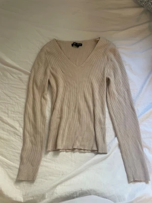 Beige ribbad tröja V-ringad - Snygg beige ribbstickad tröja med V-ringning och långa ärmar. Det är storlek L men skulle säga den passar M. Tröjan har en smal passform och är tillverkad i ett mjukt, stretchigt material som sitter skönt på kroppen. Perfekt att styla med jeans eller kjol.