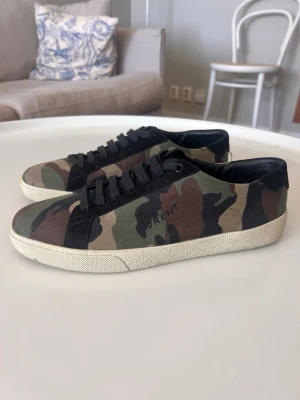 Saint Laurent camo sneakers låga - Snygga Saint Laurent court classic i ny skick  med coolt camouflagemönster i grönt, brunt och svart. Skorna har svarta snören, vit sula. Box finns med och även äkthets verifikation samt dustbag 