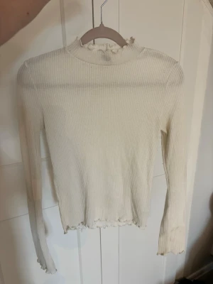 Vit ribbad långärmad topp - Säljer en vit ribbad långärmad topp med hög hals och volangkant vid halsringning och nederkant. Fler bilder finns💕