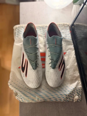 Vita Skechers fotbollsskor - Snygga vita fotbollsskor från Skechers med blått snörningsparti och röda detaljer. Skorna har en modern, strömlinjeformad design med mönstrad ovandel. Personligen så tycker jag detta är en utav om inte den skönaste fotbollskonst jag haft. Den är OTROLIGT mjuk i ovandelen och sitter som en strumpa runt foten. Propparna som sitter i höken och på hela sulan är till för att ej glida runt och minska risken för skavsår. Säljer för att jag är sugen på något nytt.