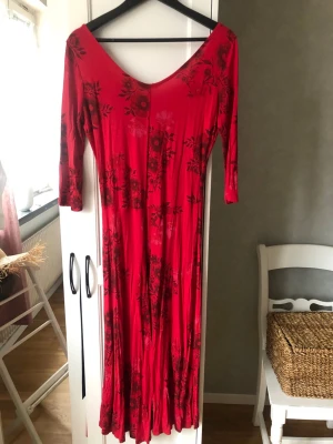 Röd långklänning från Desigual stl L - Säljer en röd långklänning i viskos från Desigual med blommigt mönster och v-ringad hals. Klänningen har trekvartsärm och är tillverkad i ett mjukt, stretchigt material som sitter snyggt på kroppen. Perfekt för dig som gillar färg och unika detaljer.