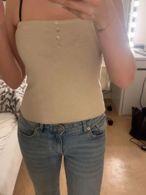 Beige ribbad tubtopp med knappar - Säljer en beige tubtopp med fyra knappar framtill. Toppen är i ett väldigt mjukt och skönt material. Passar till mycket! Aldrig använd