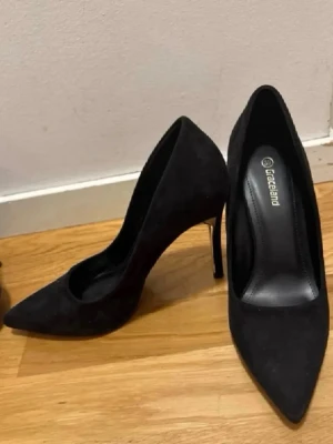 Helt NYA !!! Svarta pumps från Graceland säljes pga av har svårt med att gå med klackar. - Stilrena svarta pumps från Graceland med spetsig tå och smal guldfärgad klack. Skorna är i mockaimitation och har en klassisk siluett som ger en elegant look. Perfekta för dig som vill ha en tidlös och trendig sko med det lilla extra.