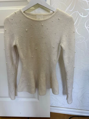 Vit ribbad topp med pärlor från H&M - Supersnygg vit ribbad topp från H&M med långa ärmar och dekorativa pärlor över hela plagget. Toppen har en figurnära passform och är perfekt för dig som gillar detaljer. Materialet känns mjukt och stretchigt.