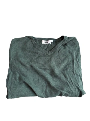 Mörkgrön V-ringad tröja golf - Mörkgrön V-ringad tröja med långa ärmar och ribbade muddar vid ärmslut och nederkant. Tröjan har en enkel och stilren design som passar till det mesta. Perfekt för dig som gillar en klassisk look.