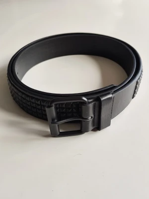 Nitbälte - Nitbälte 4 rader med små svarta pyramid nitar.  Bältet är helt nytt men passade inte mig för märkningen på skärpet är 95cm vilket inte stämmer i verkligheten.Minsta storlek runt midjan är 107cm Största storlek runt midjan är 117cm Bredd på bältet är 38mm Tjockleken på bältet är 3.9 mm (Bältets totala längd är 127cm)  När jag beställde bältet stod det att det är tillverkat av kalvskinnsläder och spaltläder. Det är ingen märkning på skärpet så jag säljer det som ett bälte av PU-läder/konstläder.