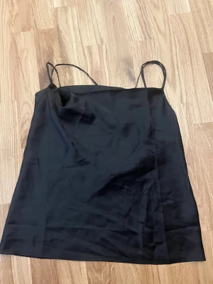 Svart linnetopp från Nelly - Snygg svart linnetopp från Nelly med tunna axelband. Material: satin