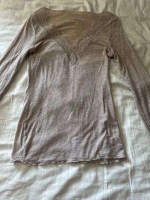 Beige långärmad topp med spets - Supersnygg beige långärmad topp med djup V-ringning dekorerad med spetsdetaljer. Tunn och mjuk kvalitet som sitter tajt mot kroppen. Perfekt att styla med jeans eller kjol för en trendig look.