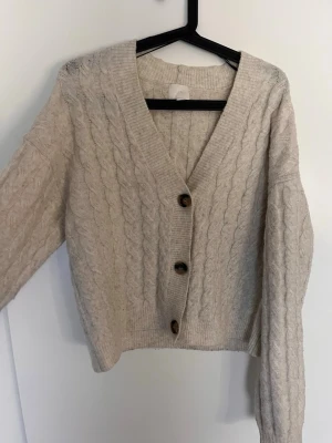 Beige kabelstickad kofta med knappar - Mysig beige kabelstickad kofta med. Perfekt att slänga över en t-shirt eller ett linne för extra värme. Materialet är väldigt mjukt å mysigt💕 storlek S men jag skulle säga att den även passar M/L 