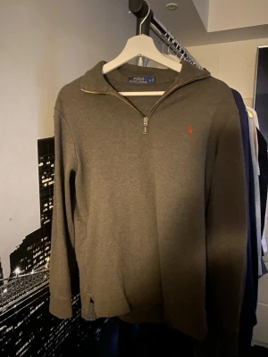 Grå halvzip från Polo Ralph Lauren - Snygg grå tröja från Polo Ralph Lauren med halv dragkedja och klassisk röd logga broderad på bröstet. Tröjan har ribbade muddar vid ärmslut och nederkant samt en mjuk bomullskänsla. Perfekt till båda vintern och sommaren!
