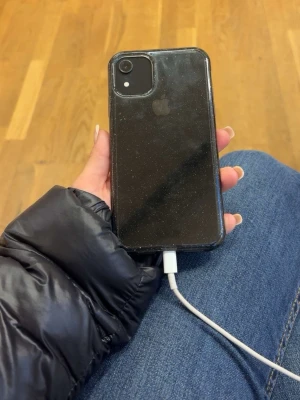 Svart iPhone med glasfront - Säljer en svart iPhone med stilren design och glasfront. Telefonen har rundade kanter och klassisk Apple-look. Perfekt för dig som gillar snygg och enkel mobil med premiumkänsla. Sen så har den en liten spricka i högra nedre hörnet, batterihälsan ligger på 90% och ljudet på telefonen är jätte bra. Skalet som sitter på får man med gratis till telefonen.